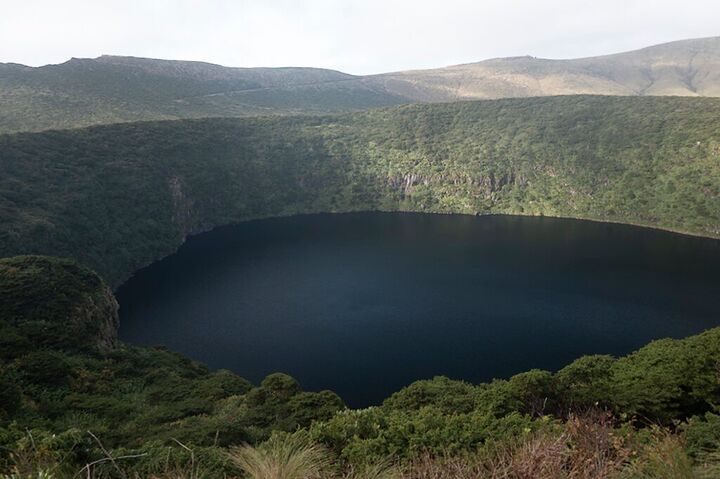 Dark crater lake ringed by green hills
