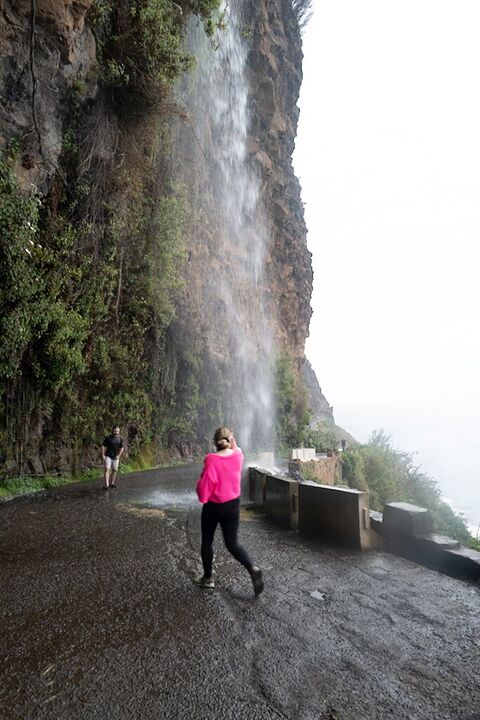 A walker in pink beneath a roadside waterfall